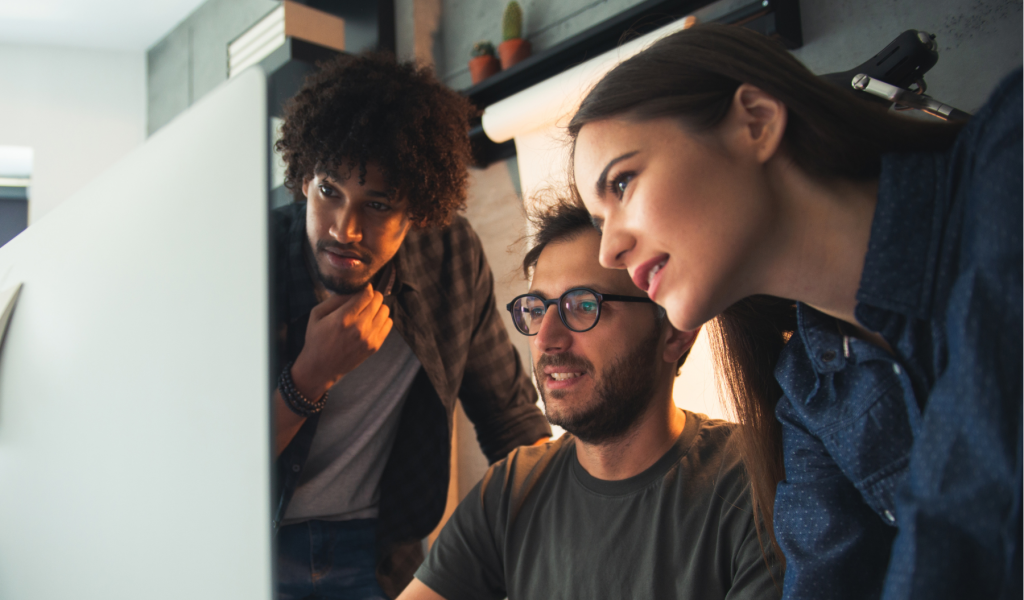 Two young men and a woman look at a computer screen together.